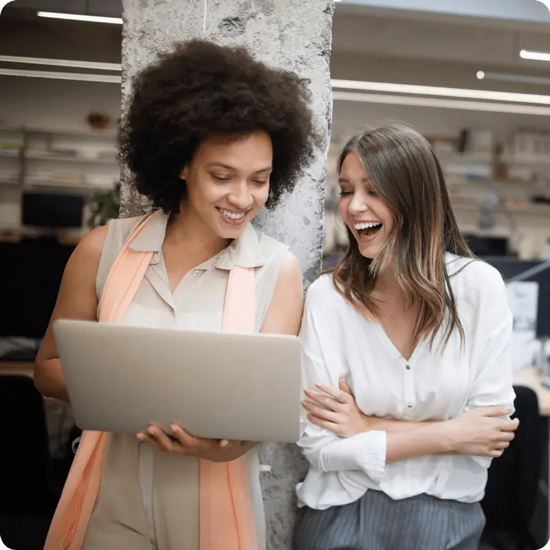 2 people smiling whilst looking at a laptop